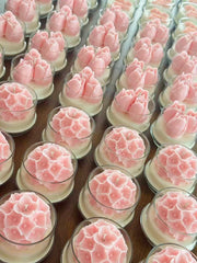 Multiple pink flower-shaped candles in clear glass holders arranged in rows on a wooden surface.