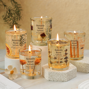 Five lit candles in glass jars labeled 'Serenity Scent by Preety' on a light surface with a neutral background.