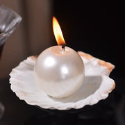 Pearl-shaped candle on a shell with a flame against a dark background